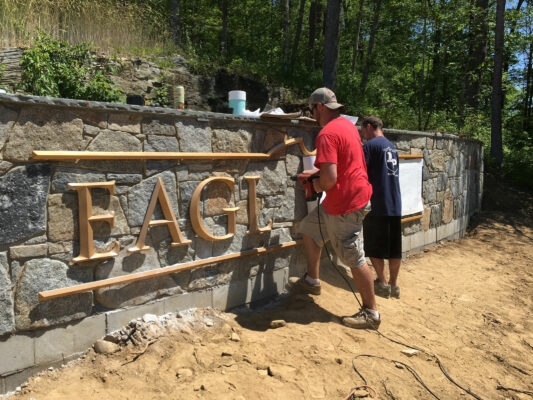 Two Men Fixing a Stone Name Board With Gold Sign